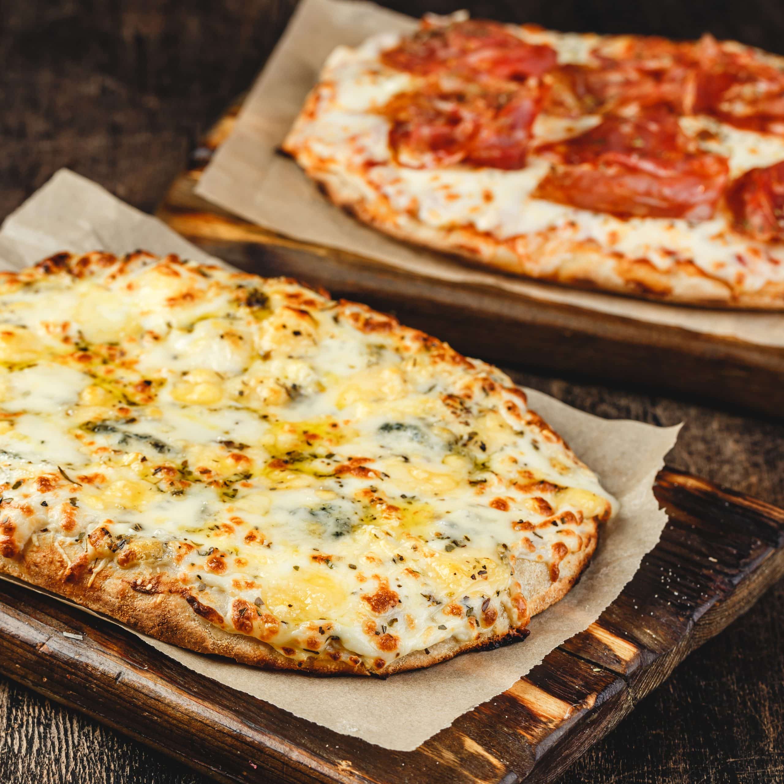 Two Roman-style pizzas with cheese and jamon serrano. Roman square pizza or Pinsa on thick dough, Italian cuisine.
